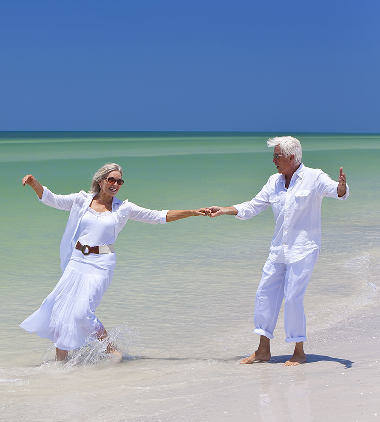 Happy Senior Couple Dancing Holding Hands On A Tropical Beach