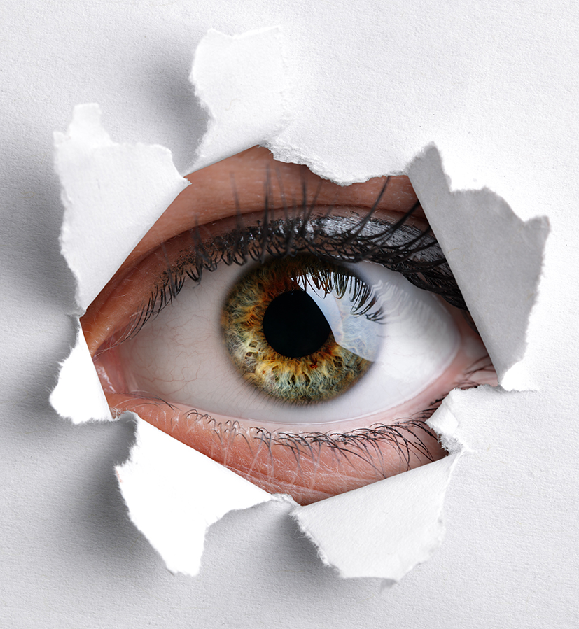 Womans eye peeking through a hole in white paper
