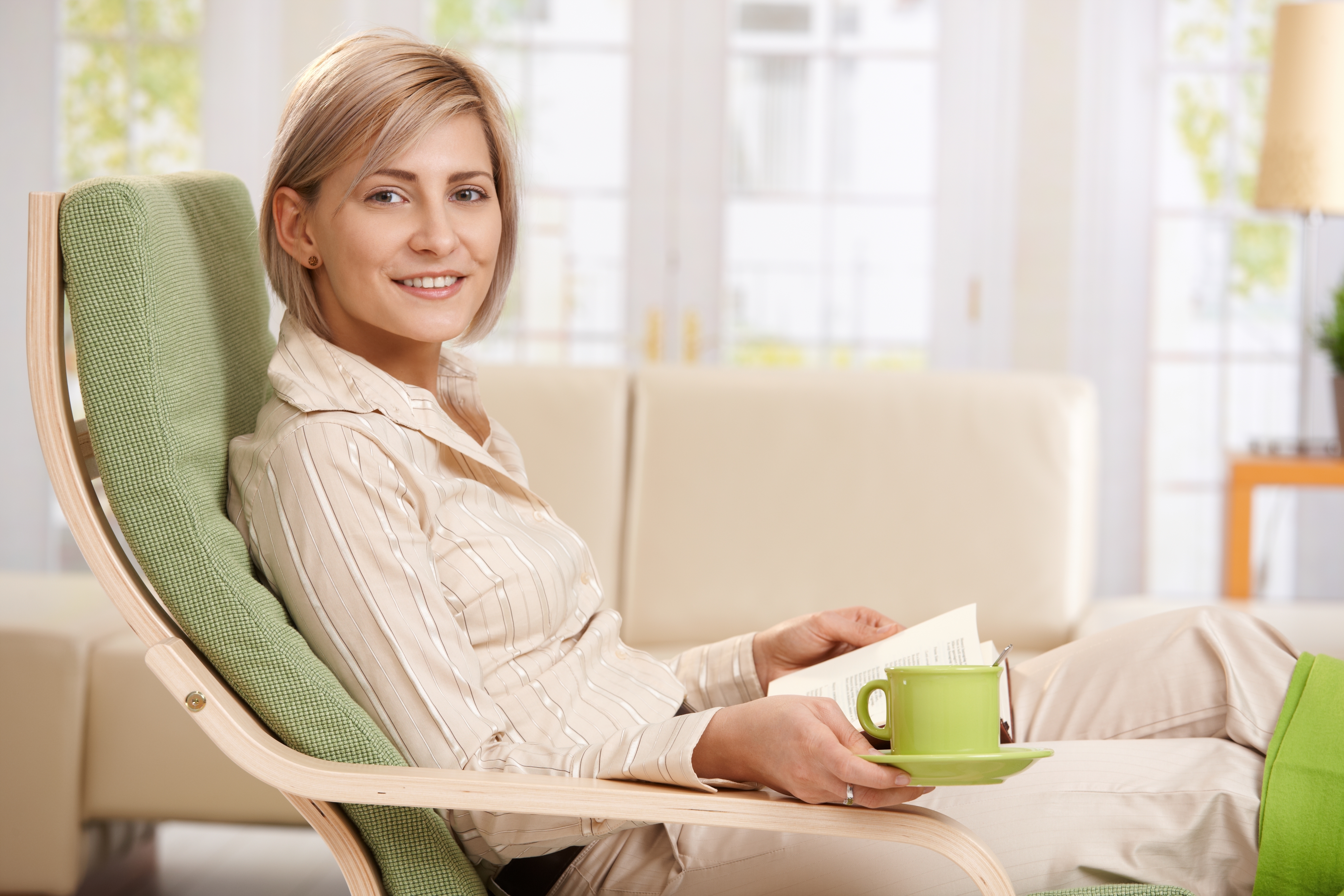 Woman relaxing in armchair at home, reading book , holding coffe